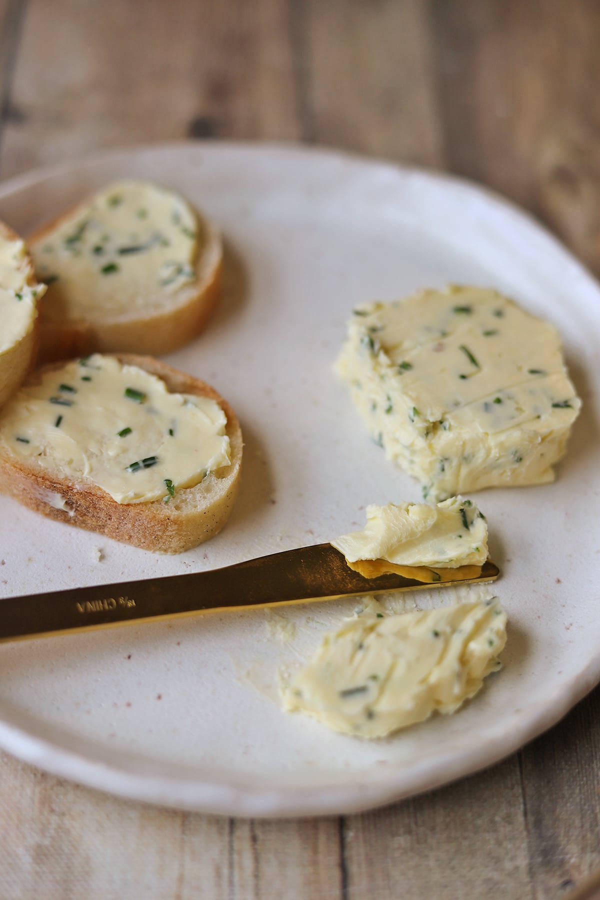 Gold knife with smear of chive and garlic butter by buttered bread.