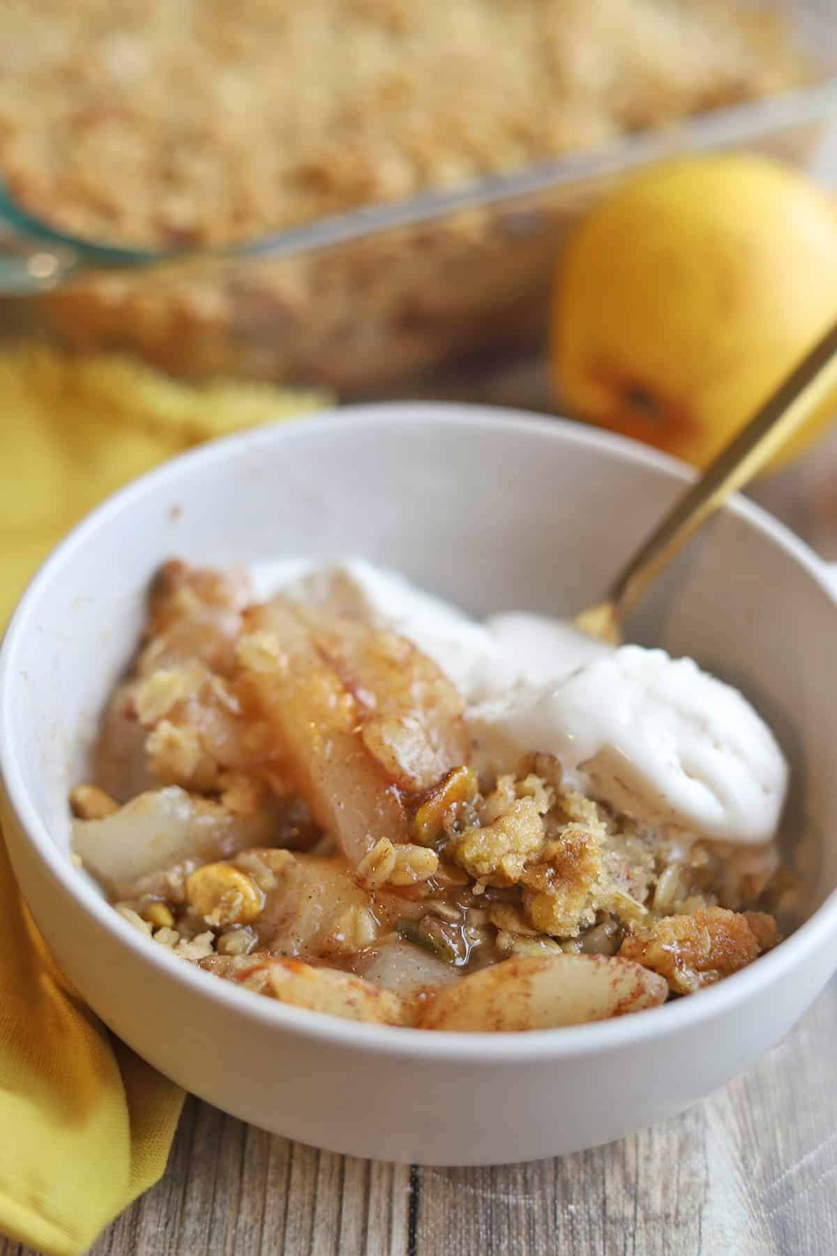 Bowl of cinnamon-covered pear crisp with melty dollops of vegan ice cream.