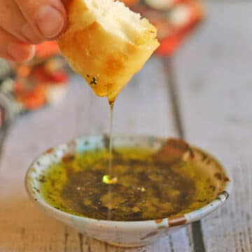 Dipping oil streaming off a piece of bread and into oil dish.