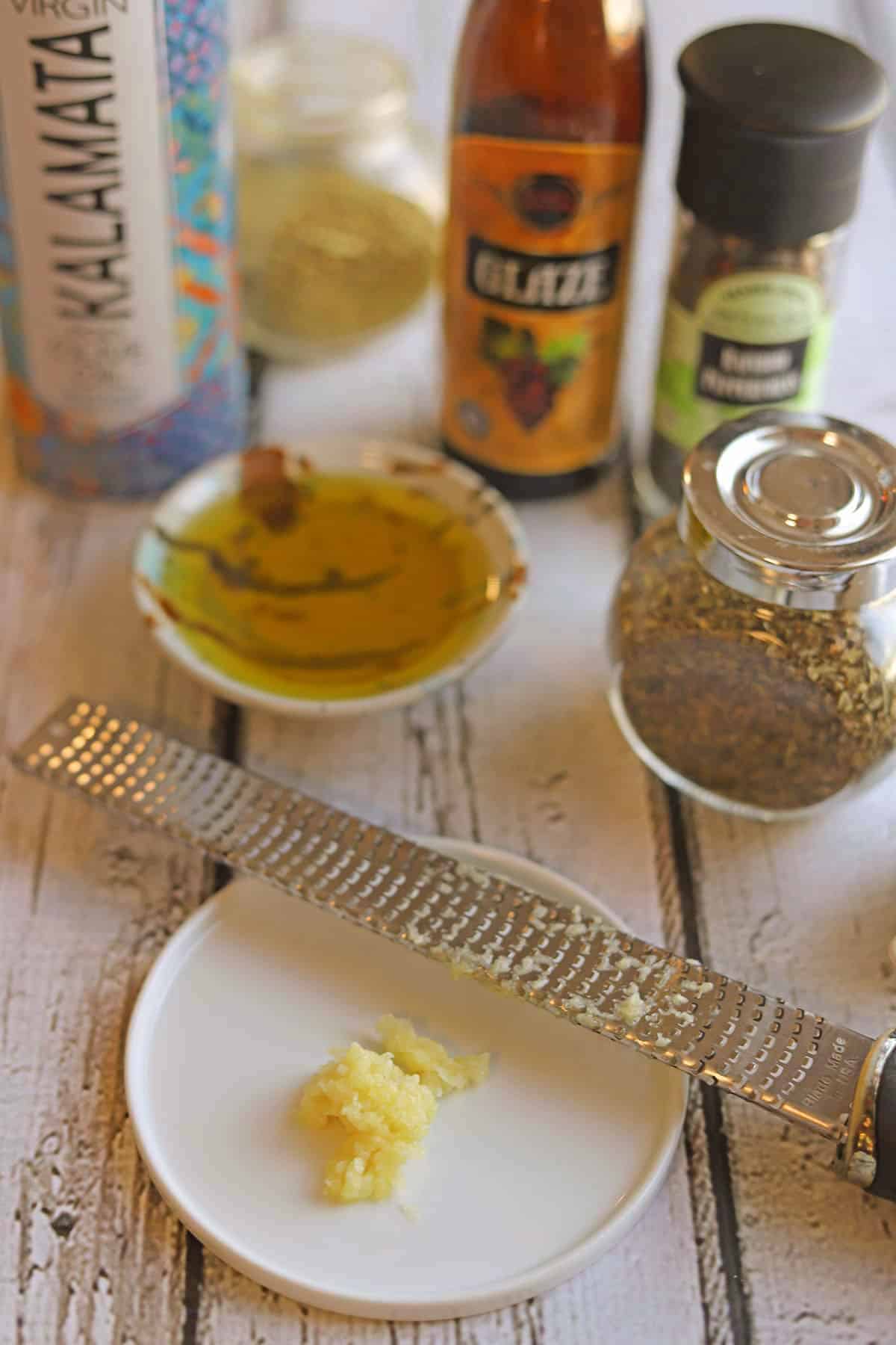 Grated garlic on plate by rasp style grater, extra virgin olive oil, balsamic glaze, and seasonings.