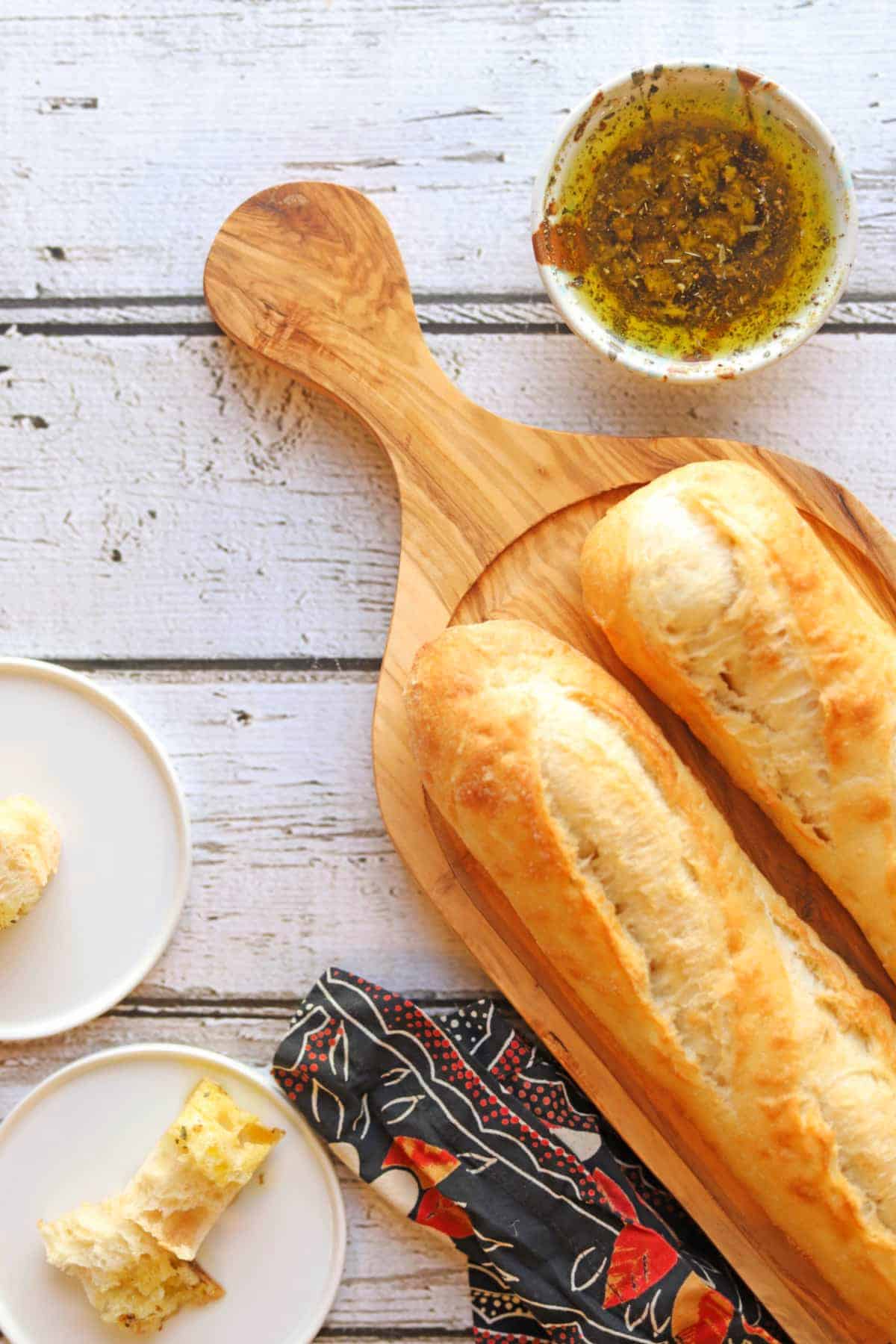 Bread dip oil in bowl by baguettes and plates with baguette pieces.