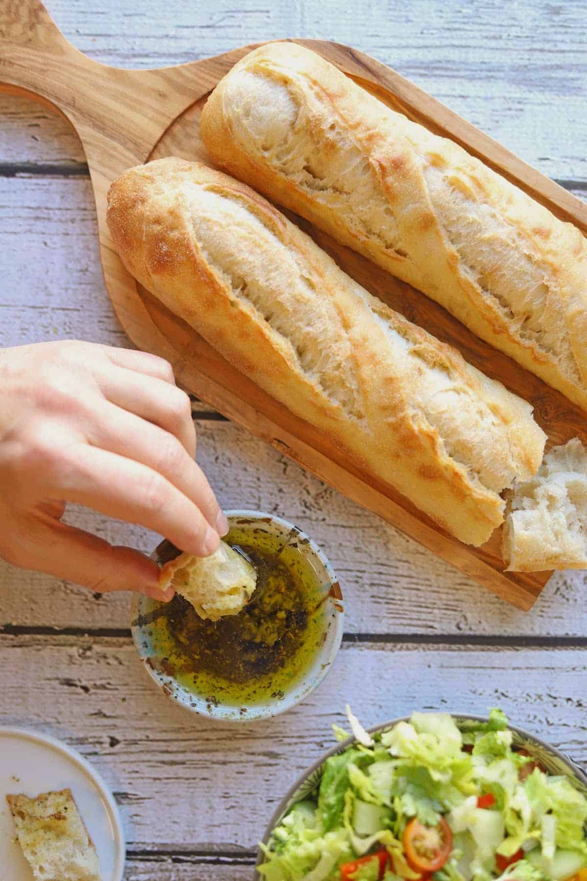 Baguettes on board by hand dunking bread into seasoned dipping oil