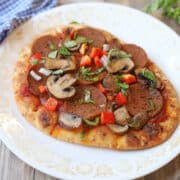 Naan flatbread pizza with mushrooms, vegan pepperoni, bell pepper, and fresh basil on white plate.