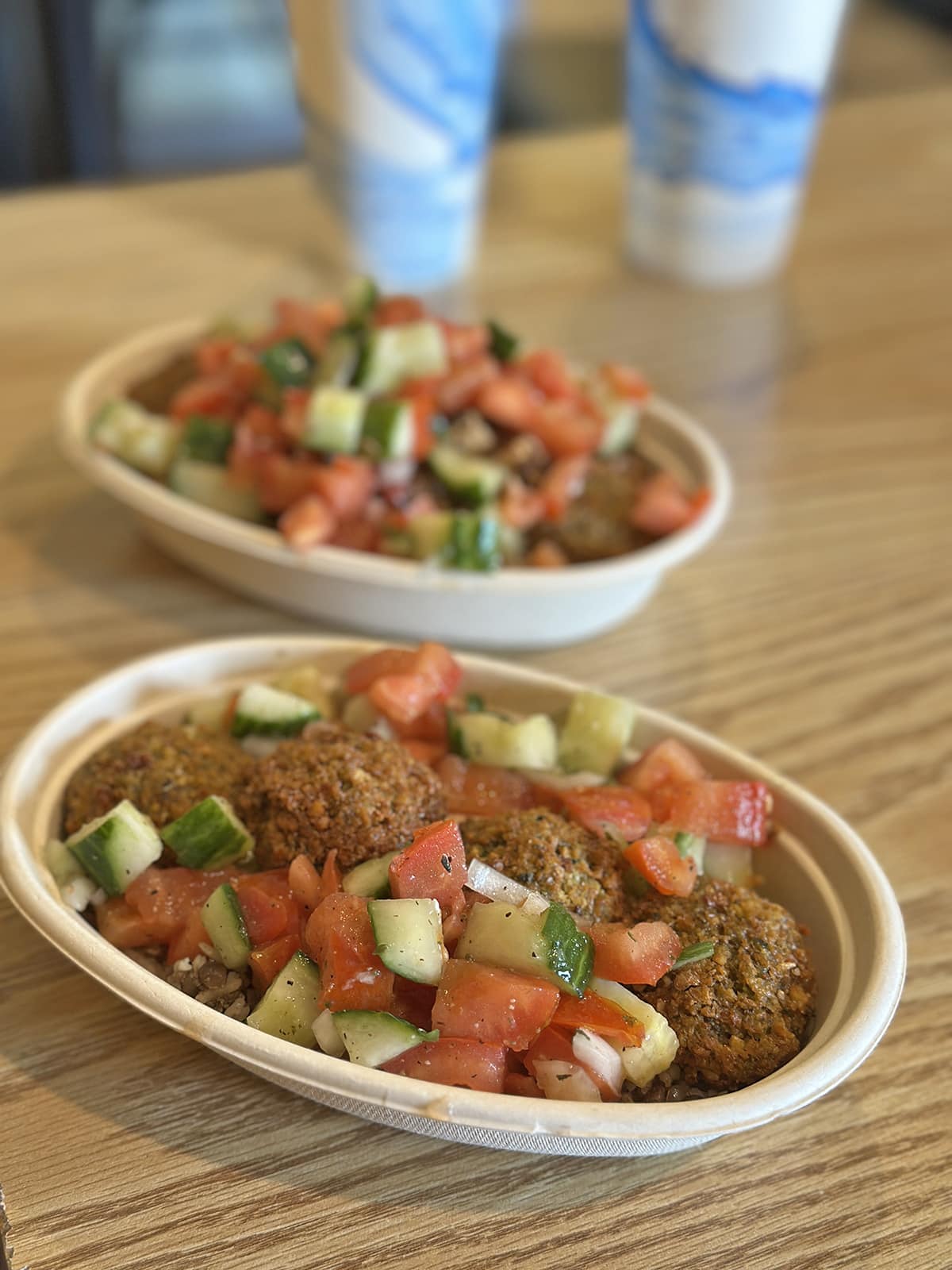 Falafel bowls with cucumber & tomato salad, rice, lentils, tofu mangal, and hummus in bowls.
