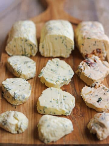 Vegan butter board with slices of dill & lemon butter, chive & garlic butter, and sun-dried tomato & basil butter.