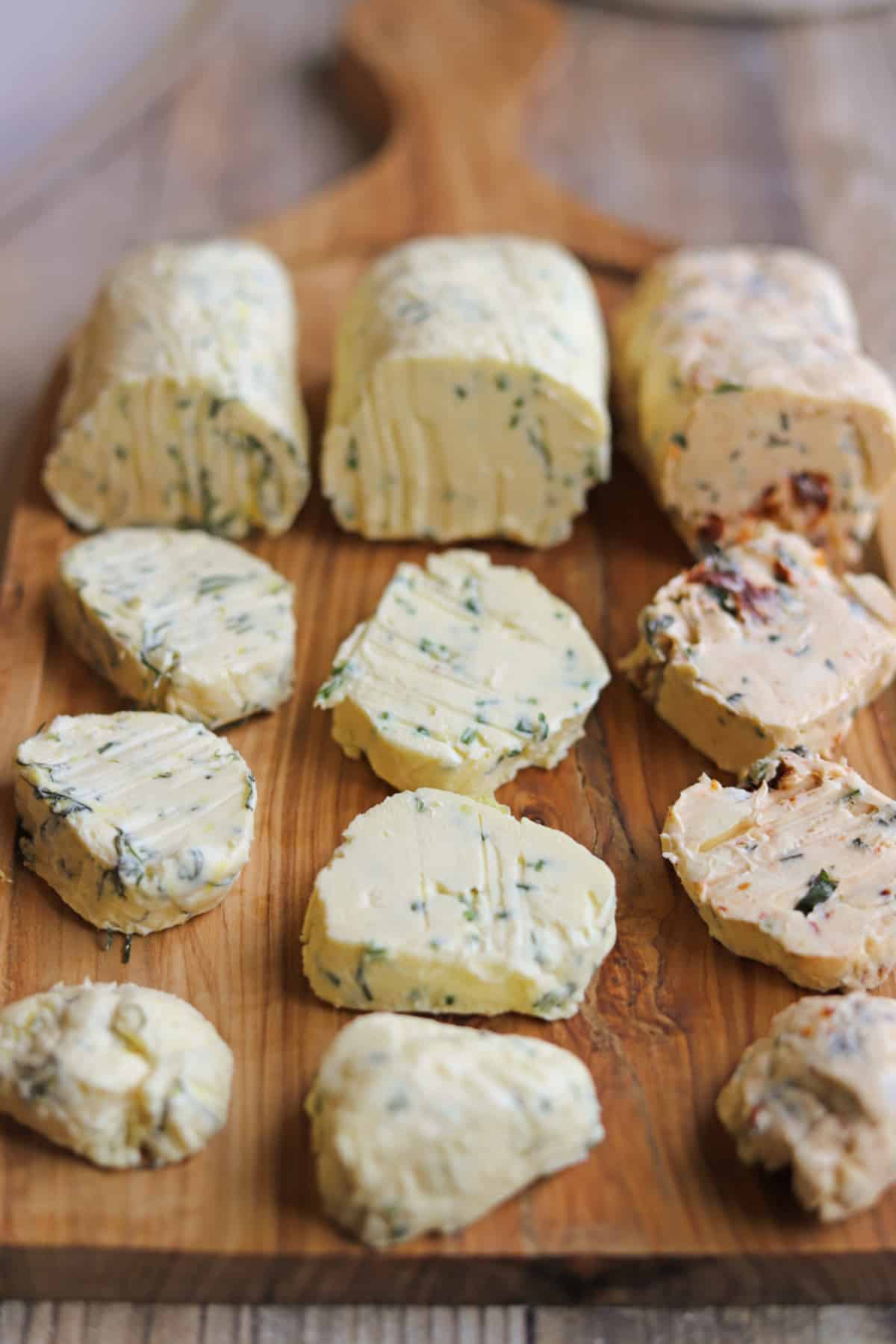 Vegan butter board with slices of dill & lemon butter, chive & garlic butter, and sun-dried tomato & basil butter.