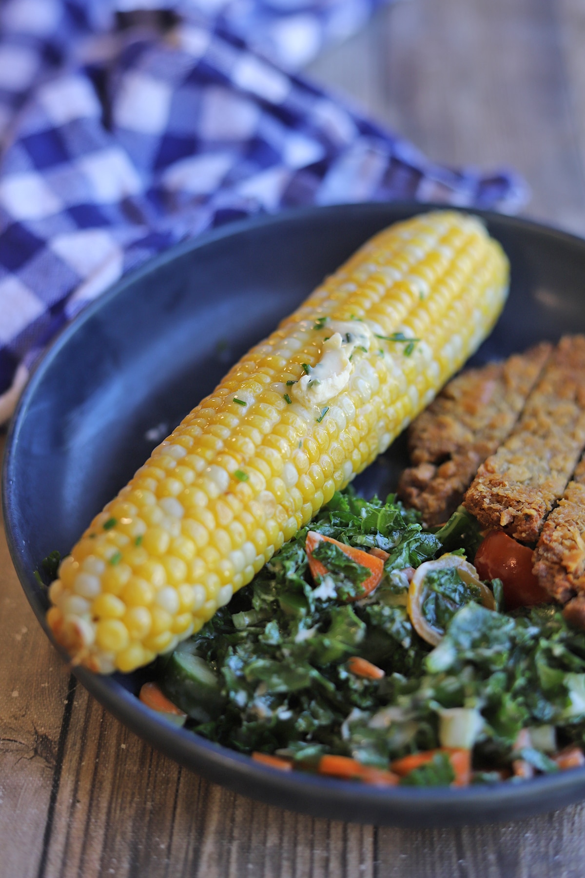 Vegan chive and garlic butter melting on ear of corn on the cob by salad and vegan schnitzel.