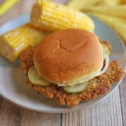 Vegan pork tenderloin sandwich with cracker breading on bun with pickles and onions by corn.