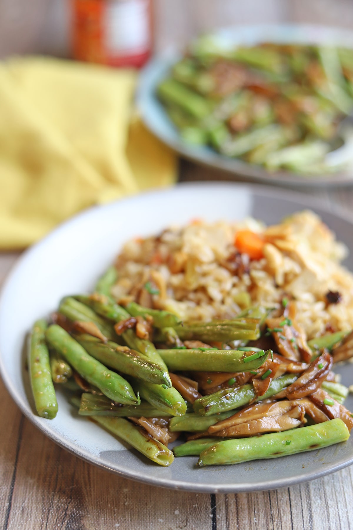 Saucy stir-fried green beans with shiitake mushrooms on plate with fried rice.