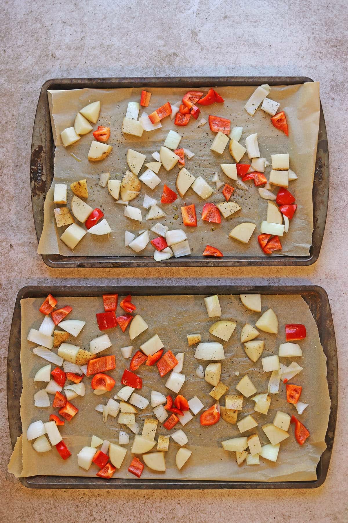 Chopped potatoes, bell pepper, and onion on two baking sheets lined with parchment paper.