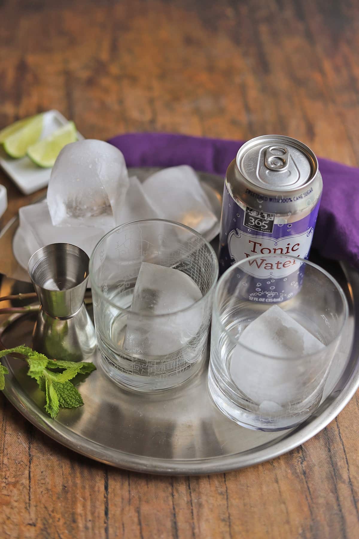 Ingredients for gin and tonic: lime wedges, tonic water, ice, gin and fresh mint by glasses with ice.