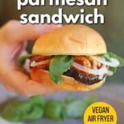 Text overlay: Eggplant parmesan sandwich, vegan air fryer recipe, get the recipe at cadryskitchen.com. Hand holding vegan eggplant parm.
