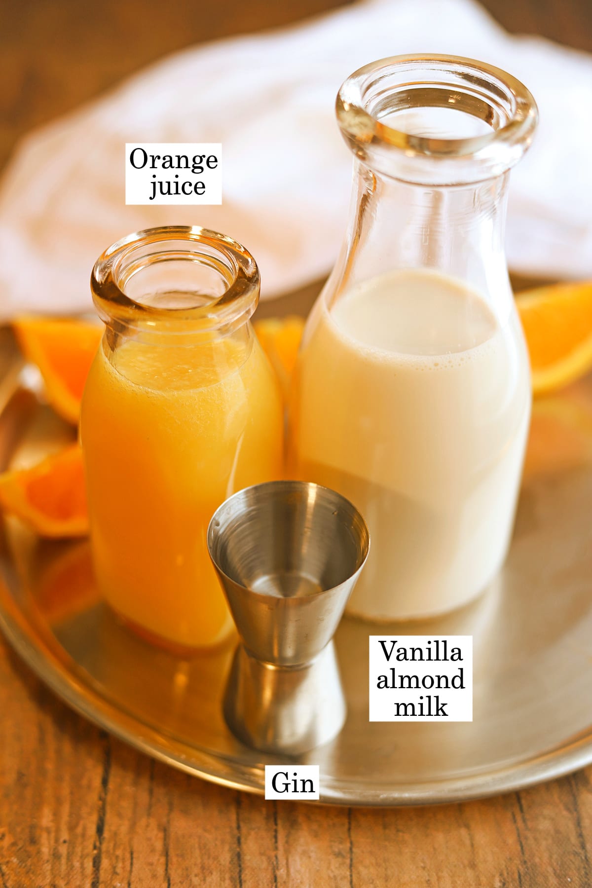 Labeled ingredients for orange creamsicle cocktail: freshly squeezed orange juice, non-dairy vanilla almond milk, and a shot of gin.
