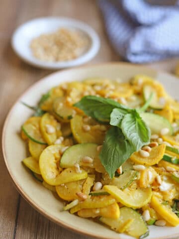 Garlicky zephyr squash and zucchini on plate garnished with fresh basil.