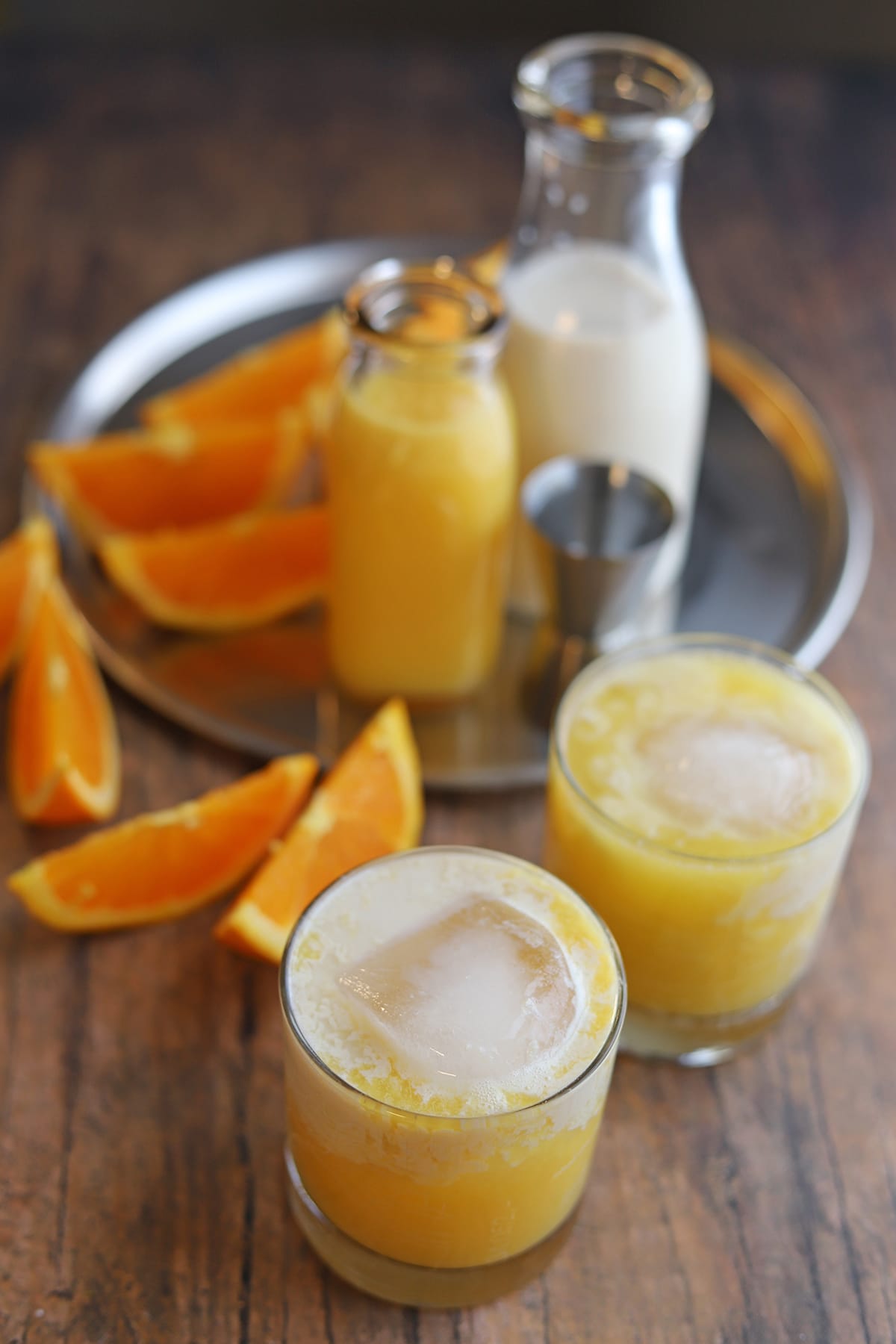 Orange creamsicle cocktail in glasses by orange slices, non-dairy milk, gin, and fresh squeezed orange juice.