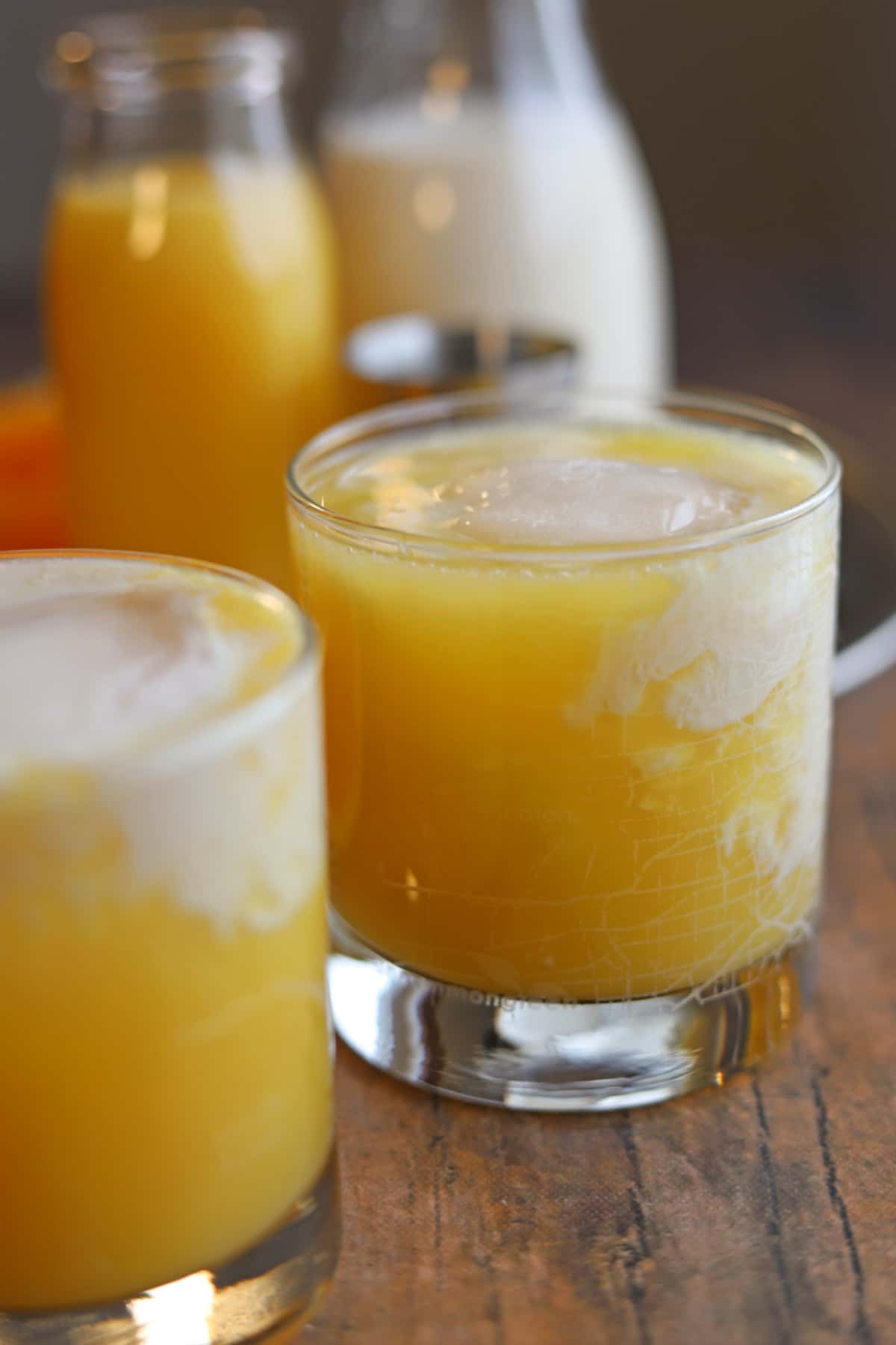 Glasses of orange creamsicle cocktail with swirls of almond milk.