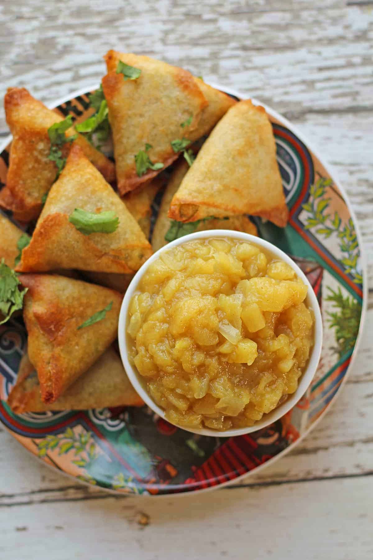 Apple chutney in bowl with samosas.