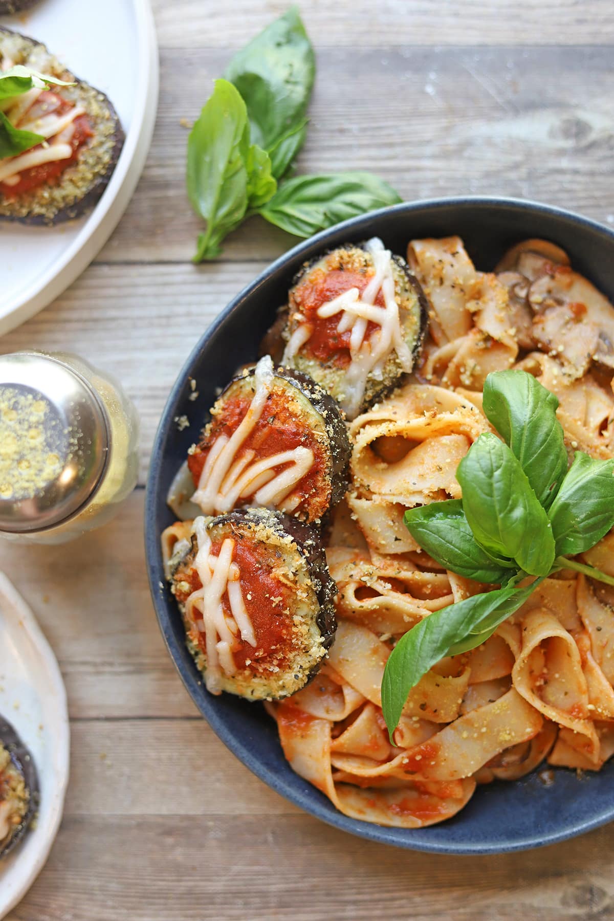 Vegan eggplant parmesan on bowl of noodles with fresh basil.