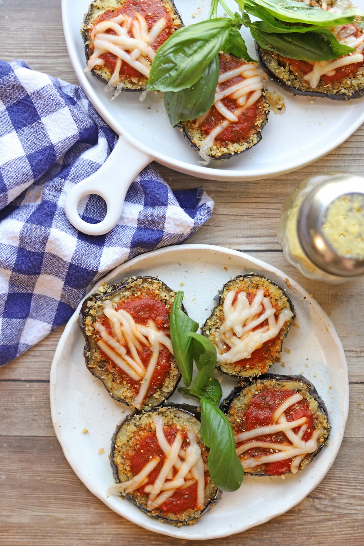 Air fryer eggplant parmesan rounds on plates with fresh basil.