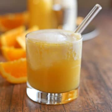 Orange creamsicle cocktail with gin, orange juice, and almond milk in glass with straw.