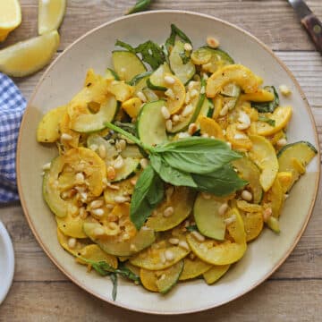 Slices of cooked yellow squash and zucchini on plate, topped with fresh basil.