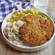 Vegan schnitzel crusted in saltines on plate with mashed potatoes and sauteed summer squash.