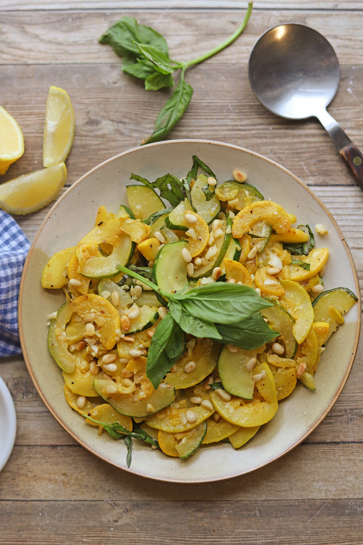 Lemony zucchini and summer squash with fresh basil and toasted pine nuts on plate by serving spoon.