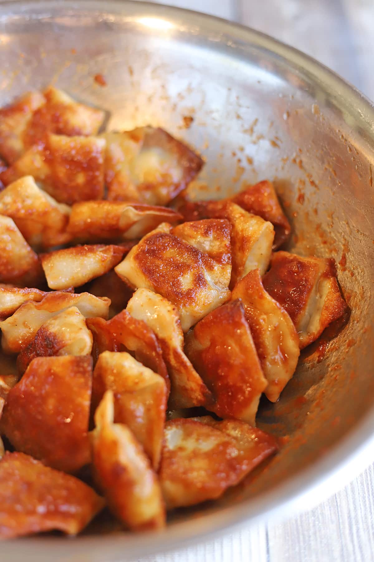 Fried tofu dumplings tossed in adobo sauce in mixing bowl.
