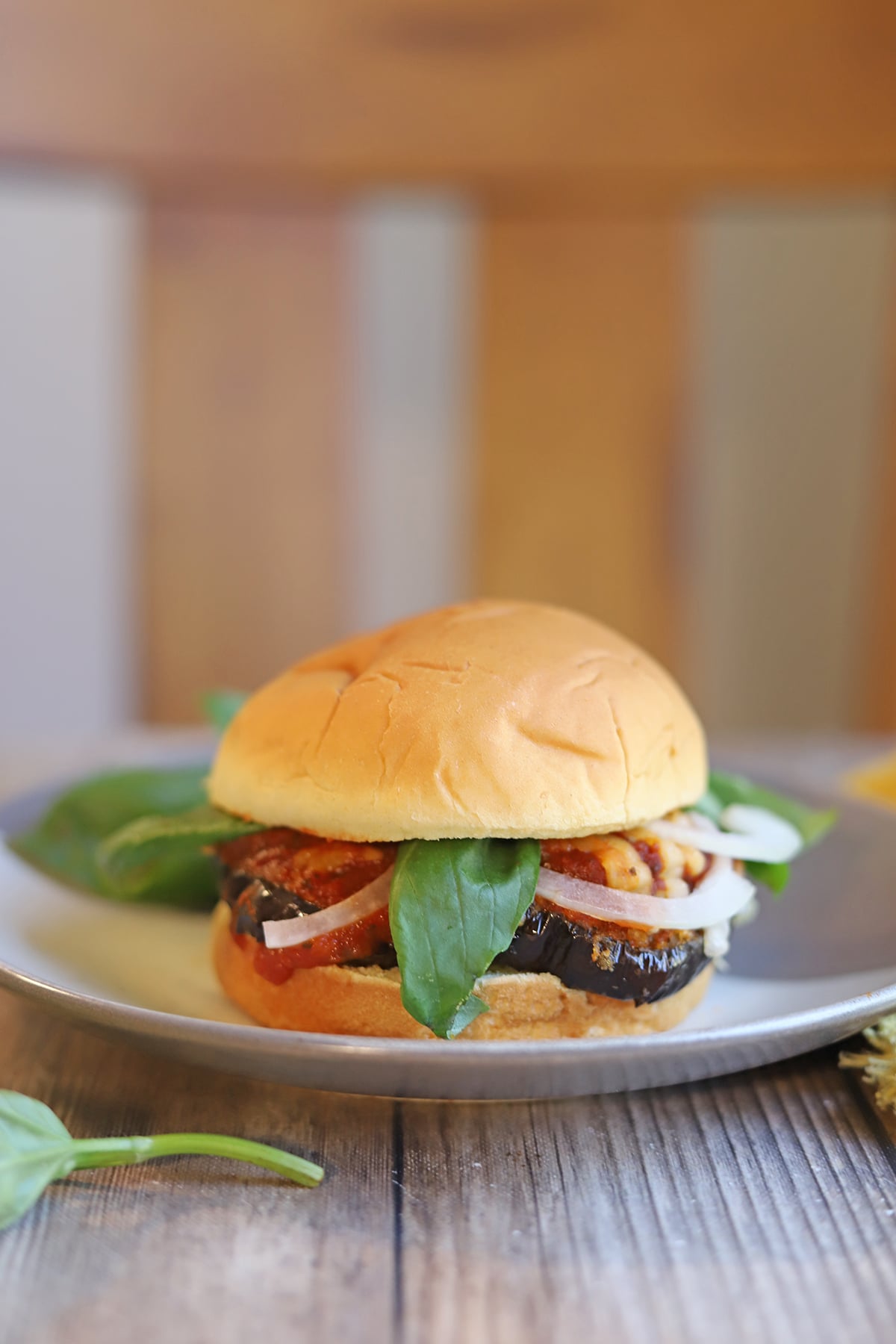 Breaded eggplant sandwich on plate with fresh basil and marinara.