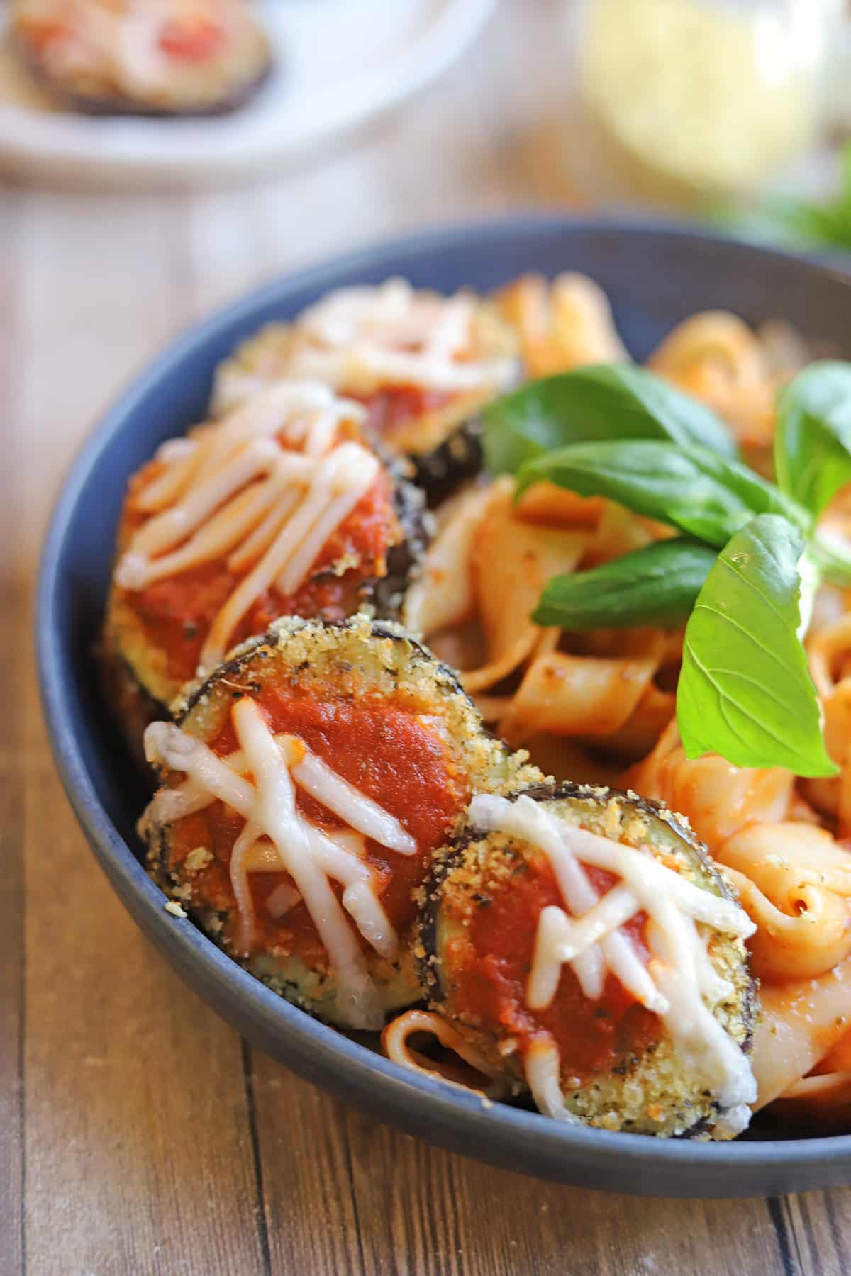 Breaded eggplant cutlets with marinara and non-dairy cheese on bowl of pasta.