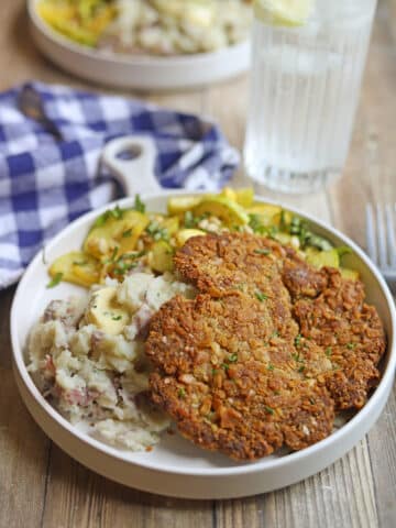 Crispy pan-fried vegan schnitzel on plate with mashed potatoes and sauteed squash.