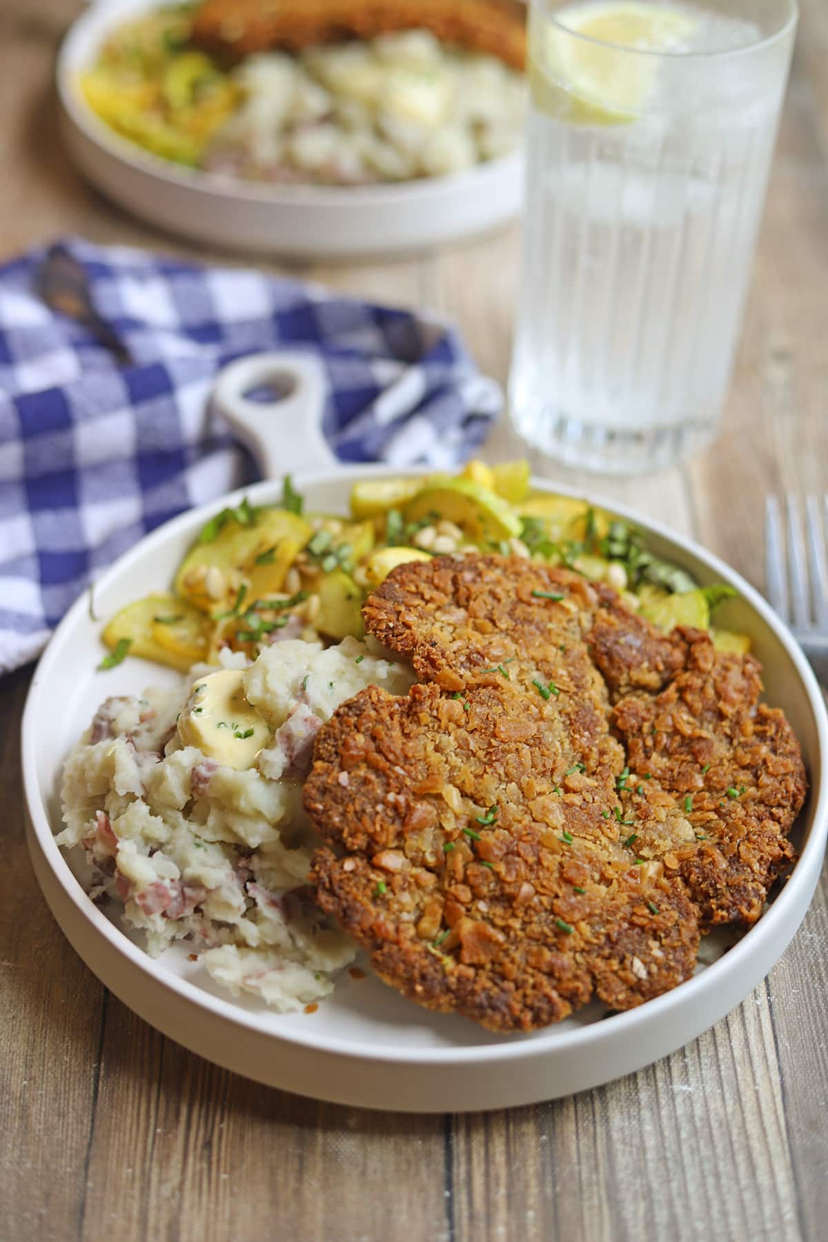 Crispy pan-fried vegan schnitzel on plate with mashed potatoes and sauteed squash.