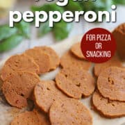 Text overlay: Vegan pepperoni, for pizza or snacking, get the recipe at cadryskitchen.com. Sliced seitan pepperoni on cutting board by fresh basil.