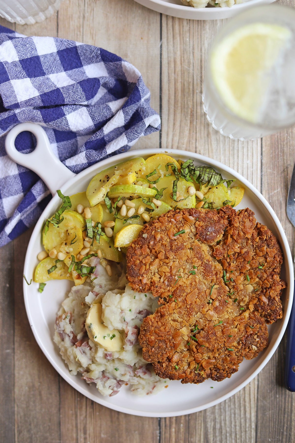 Breaded seitan and chickpea cutlet on plate with sauteed squash and mashed potatoes.