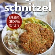 Text overlay: Vegan schnitzel, breaded chickpea cutlets, get the recipe at cadryskitchen.com. Breaded plant-based schnitzel on plate with mashed potatoes and zucchini.