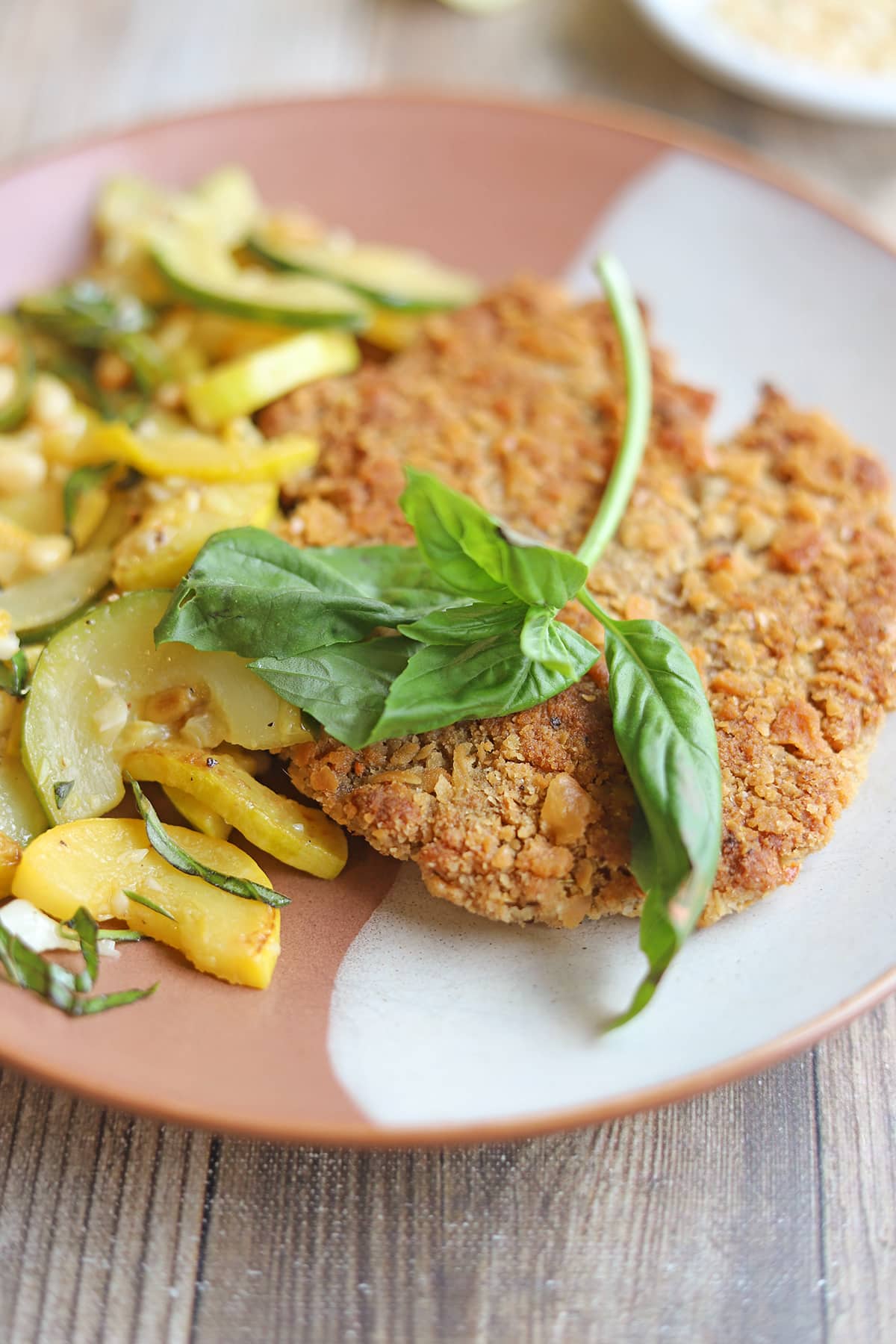 Breaded vegan cutlet on plate with sauteed summer squash and zucchini.