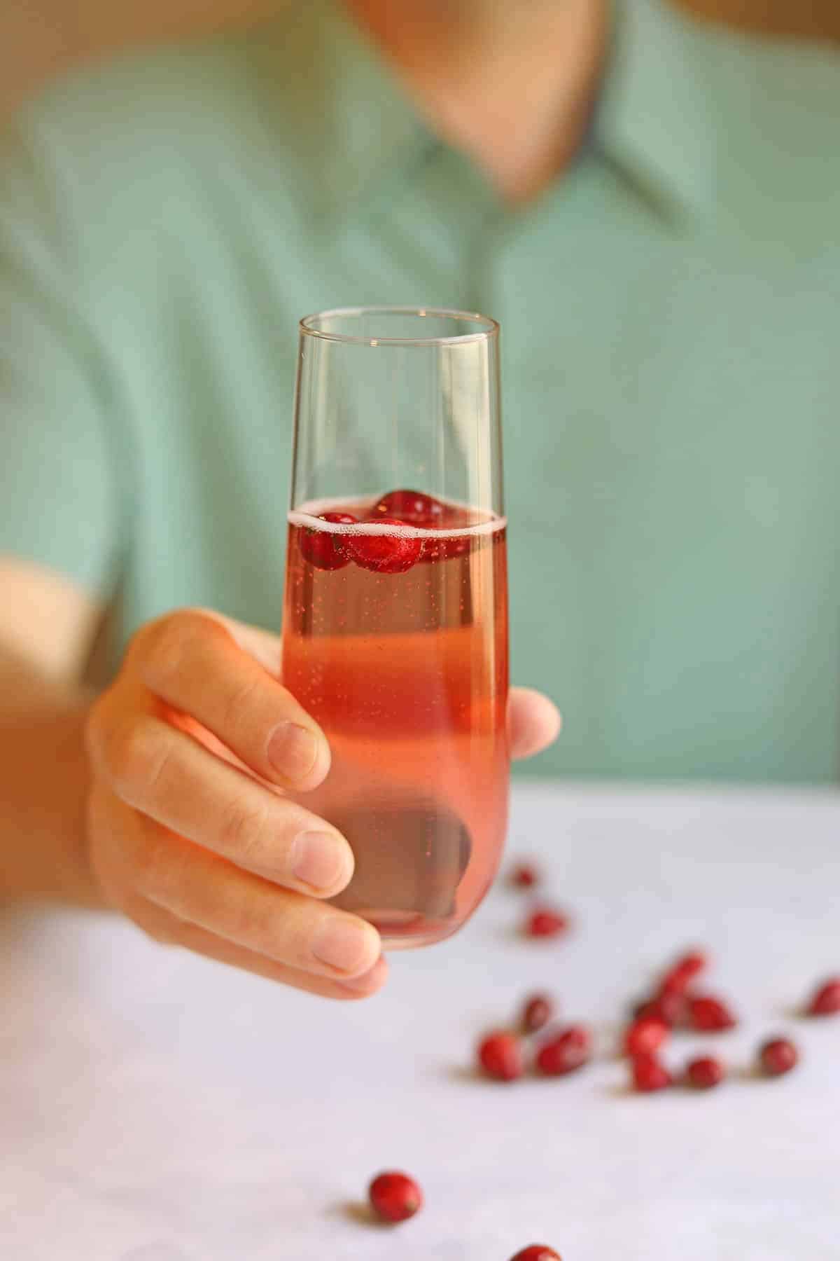 Hand holding glass of easy cranberry mimosa with fresh cranberries and cranberry juice.