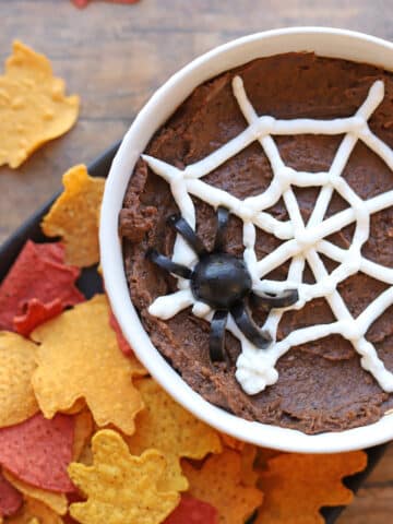 Halloween dip with chipotle black beans, non-dairy sour cream spider web, olive spider, and leaf tortilla chips.