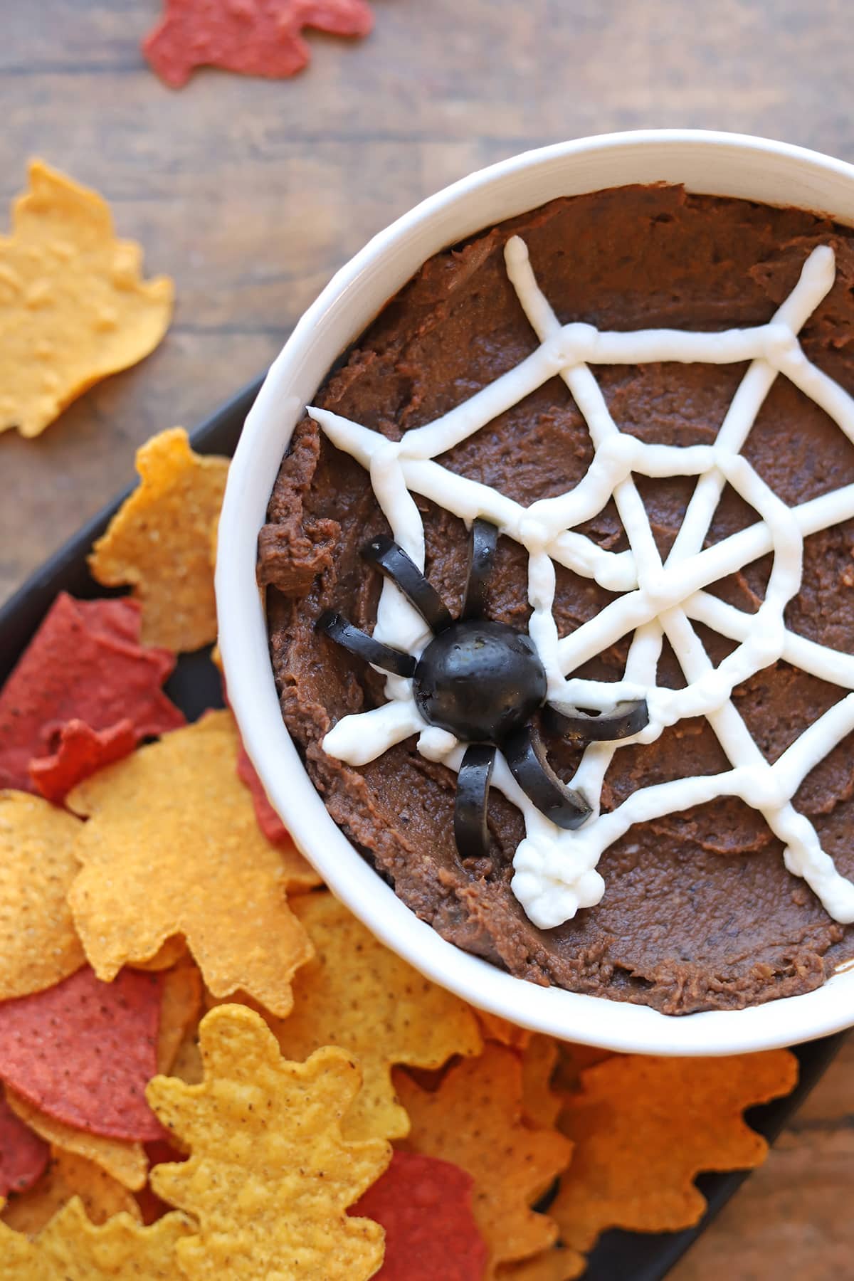 Halloween dip with chipotle black beans, non-dairy sour cream spider web, olive spider, and leaf tortilla chips.
