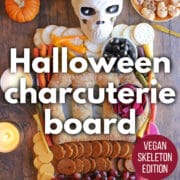 Text overlay: Halloween charcuterie board, vegan skeleton edition, get the recipe at cadryskitchen.com. Skeleton charcuterie on table by candles and pumpkins.