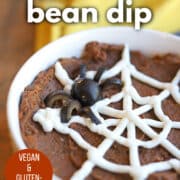 Text overlay: Halloween bean dip, vegan and gluten-free, get the recipe at cadryskitchen.com. Vegan sour cream spider web and olive spider on bowl of bean dip.