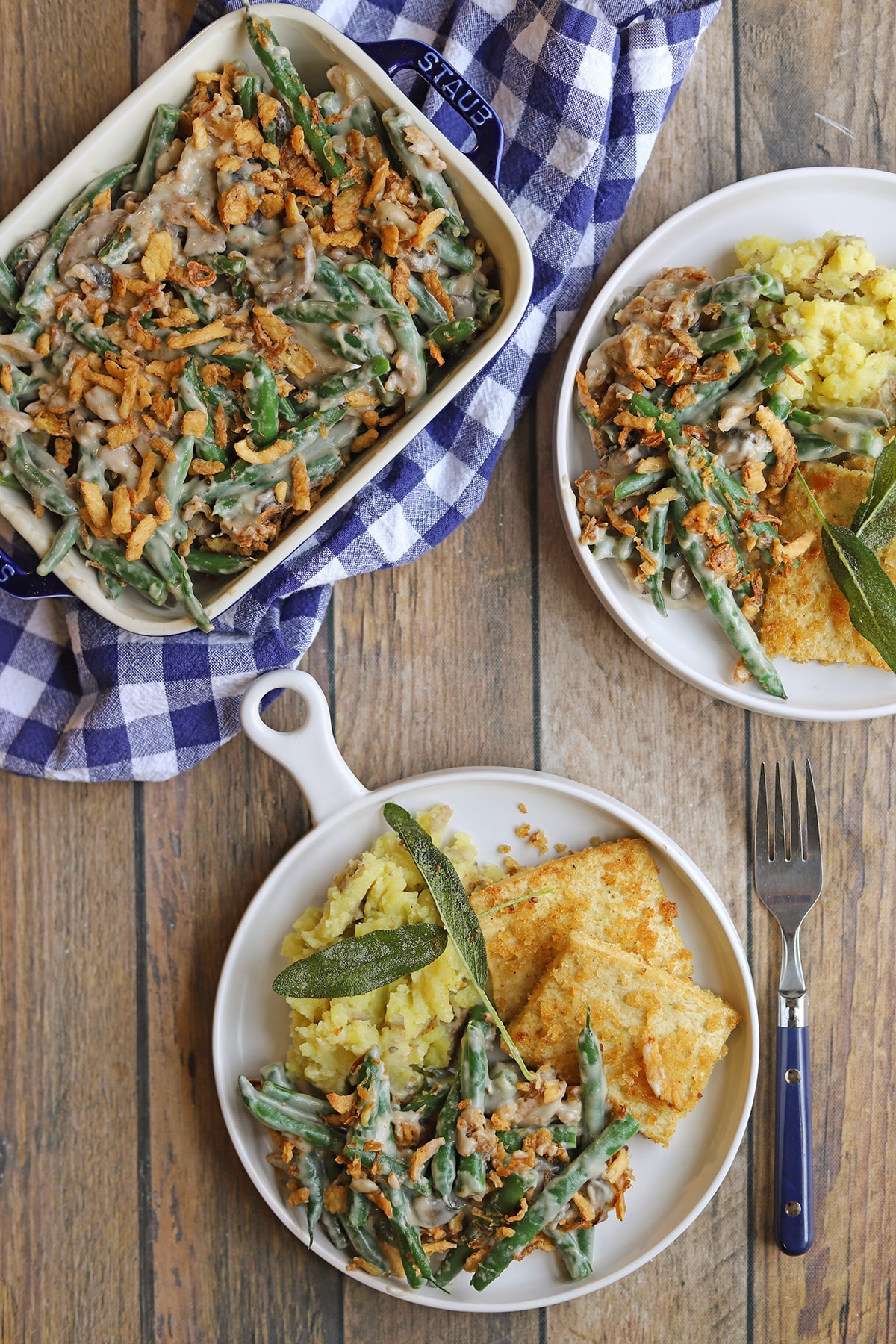 Vegan green bean casserole in serving dish by Thanksgiving plates with mashed potatoes, fried tofu, and green bean casserole.