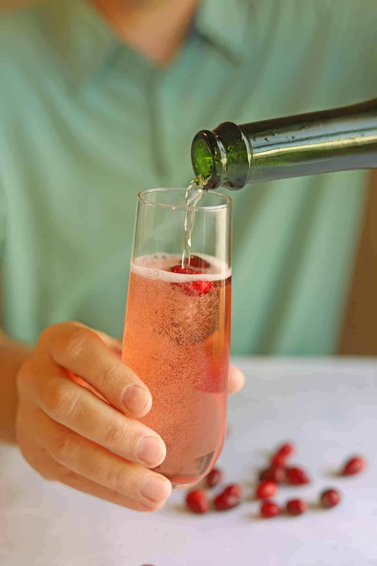 Pouring champagne into glass with cranberry juice and cranberries.