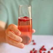 Hand holding cranberry mimosa, easy holiday cocktail, with floating cranberries in glass.