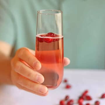 Hand holding cranberry mimosa, easy holiday cocktail, with floating cranberries in glass.