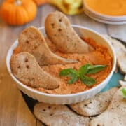 Crispy pita ghosts in bowl of hummus with basil garnish.