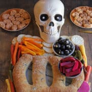 Skull with olive eyes smiling on skeleton charcuterie board.