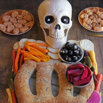 Skull with olive eyes smiling on skeleton charcuterie board.