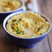 Southern-style vegan grits with melted non-dairy butter and chives in blue bowl.