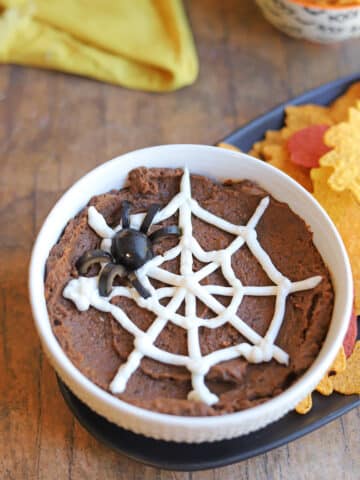 Halloween dip with vegan sour cream spider web and black olive spider in bowl by tortilla chips.